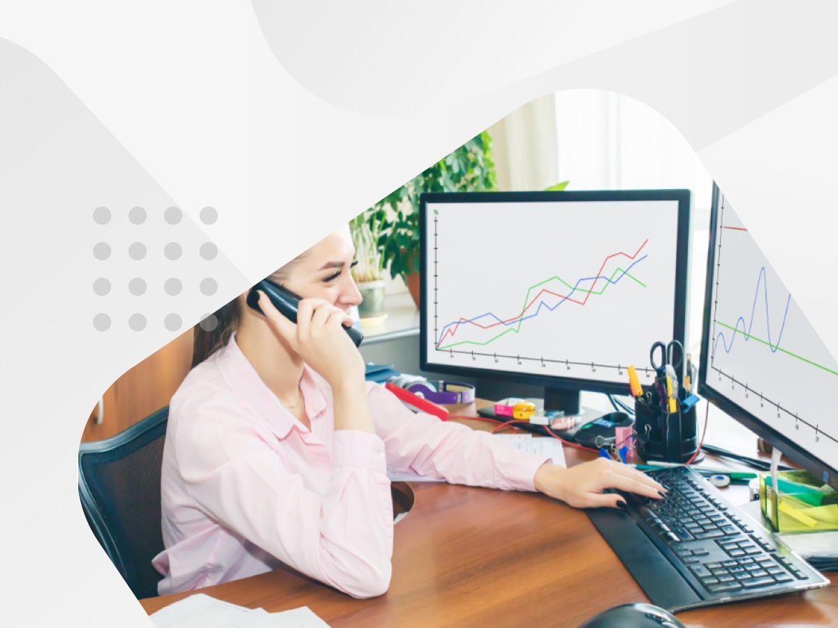 A woman sitting at a desk with two monitors and a phone