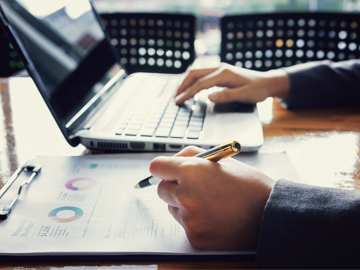 A businessman's hands multitasking with a pen and laptop, jotting down notes and working on important documents.