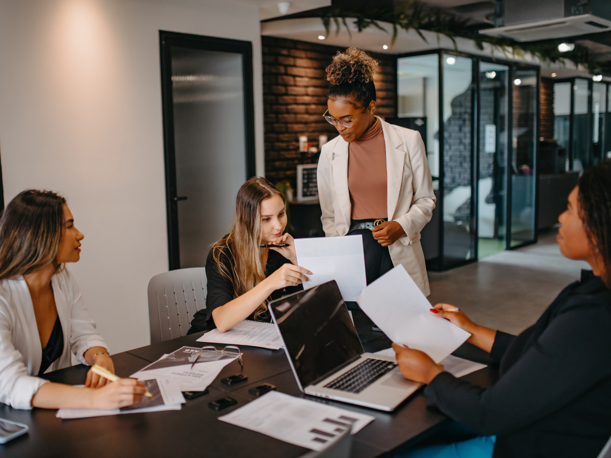 Four professional women discussing in a modern office setting.